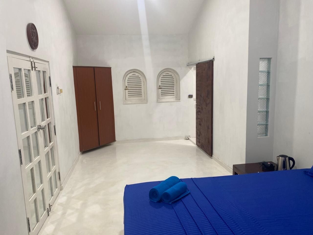A room with a bed, a wardrobe, a door, and a small table with a kettle.