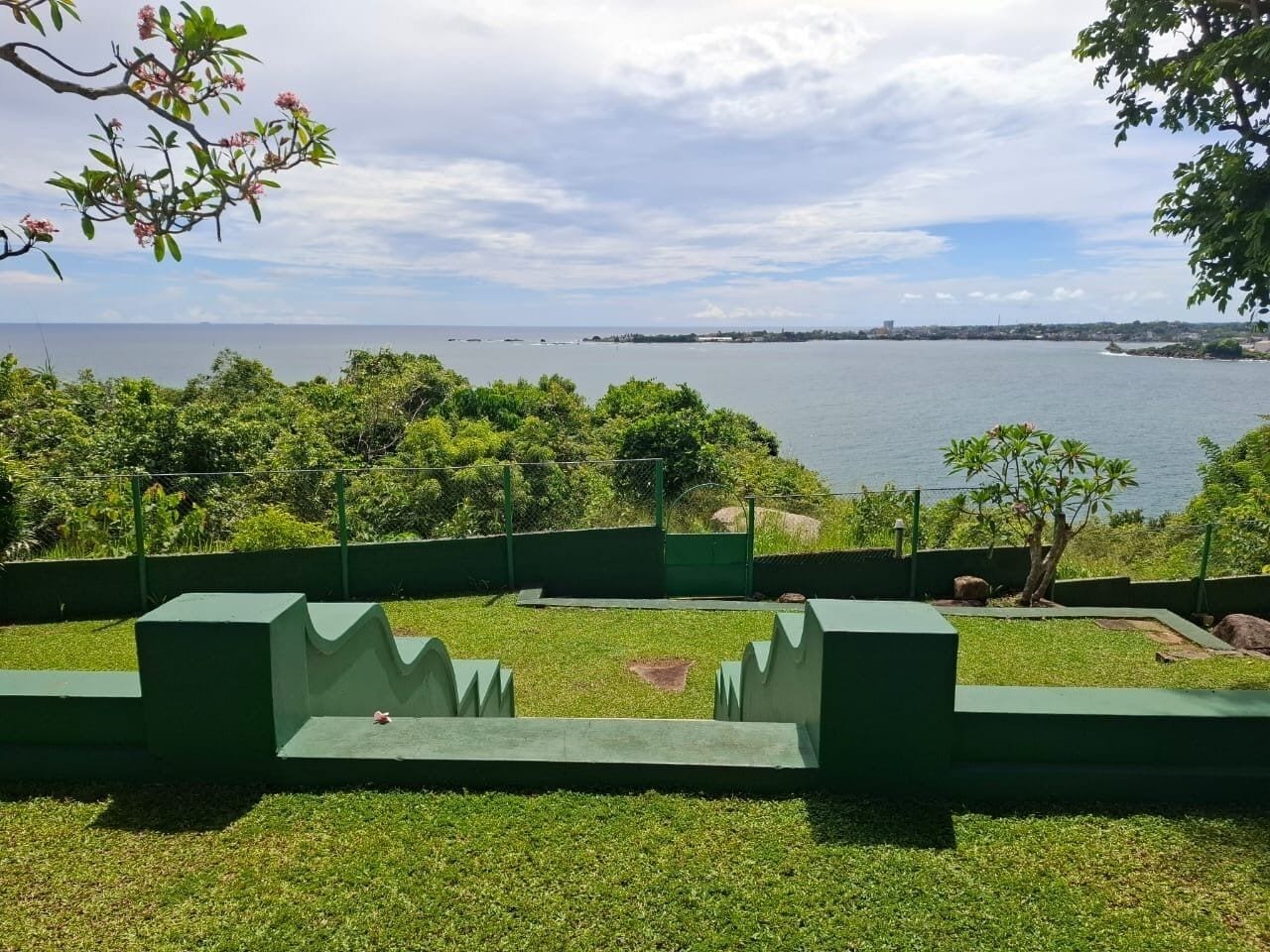 Un parc avec des allées verdoyantes, un petit étang et une vue sur la mer.