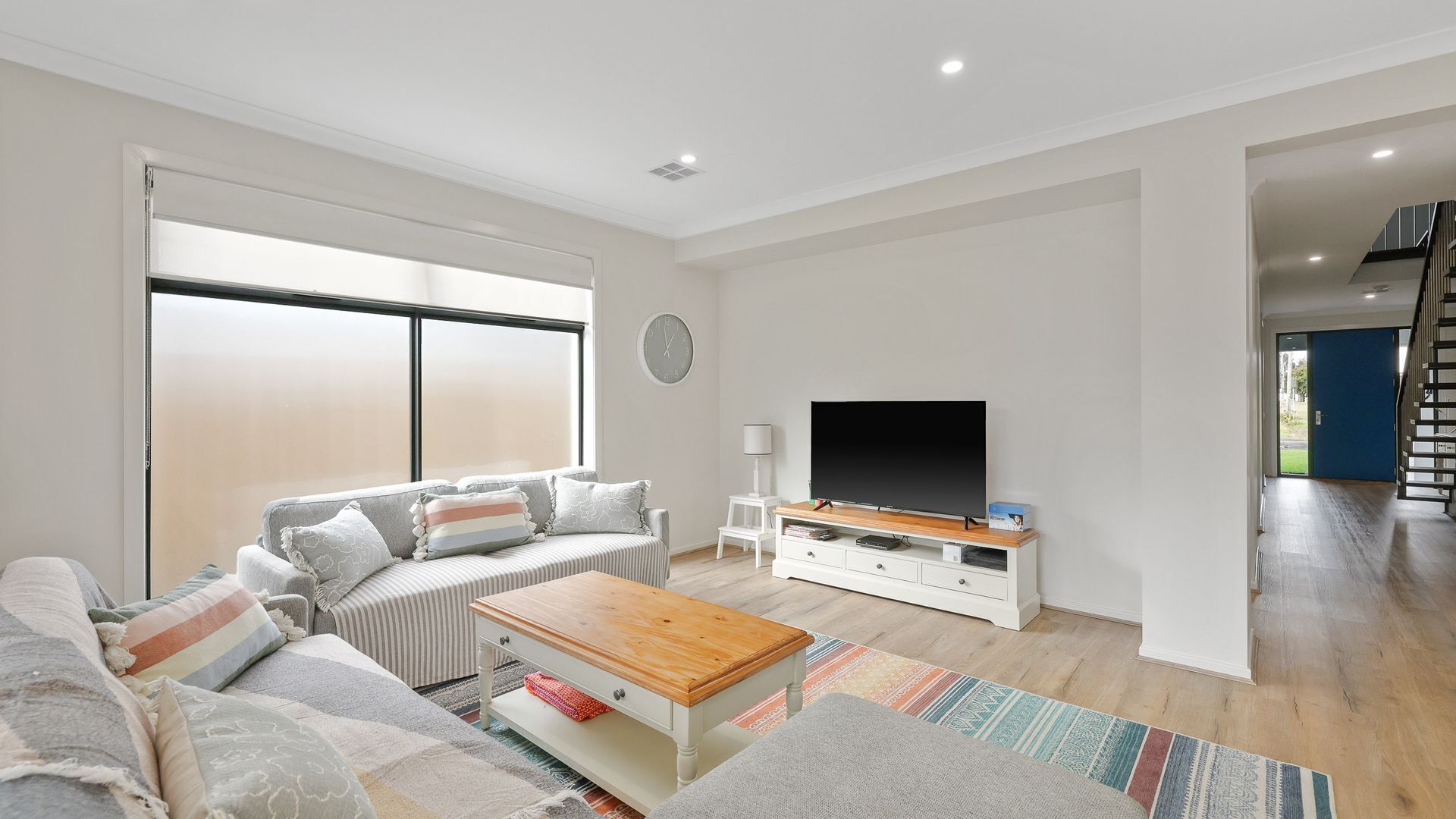 A modern living room with a sofa, coffee table, TV, and a staircase leading to another level.