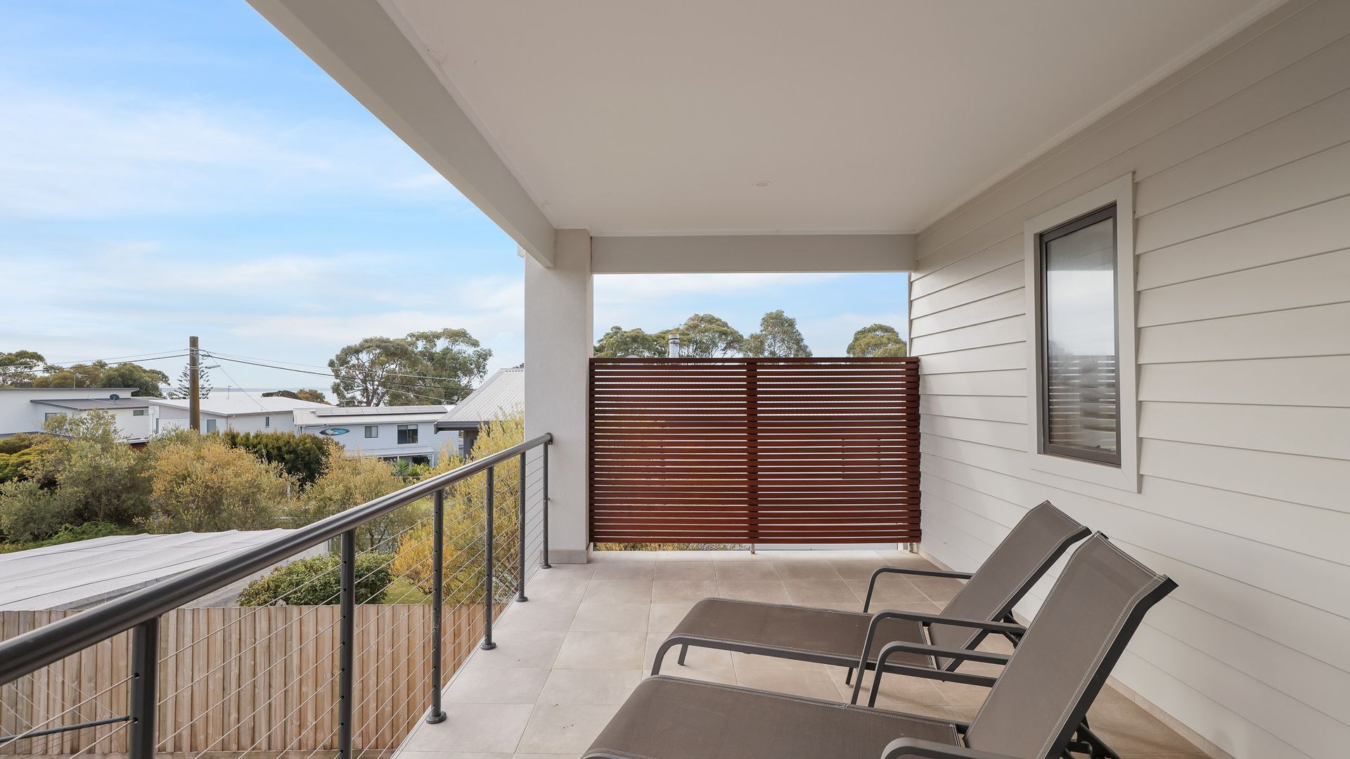A balcony with two lounge chairs, a wooden fence, and a view of neighboring houses.