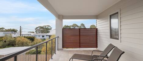 A balcony with two lounge chairs, a wooden fence, and a view of neighboring houses.