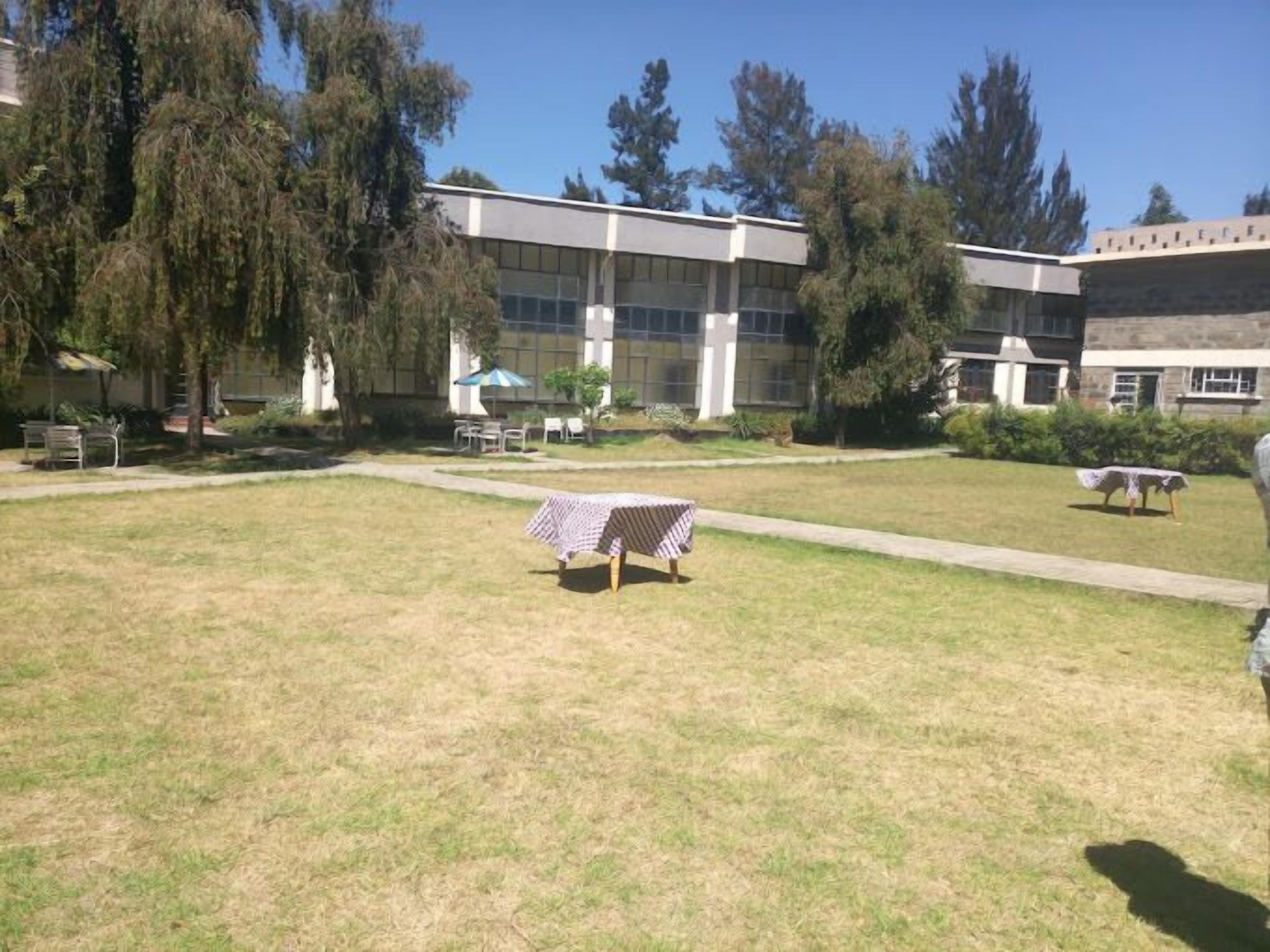 A grassy courtyard with a picnic table and chairs, surrounded by buildings with large windows and a cross structure.