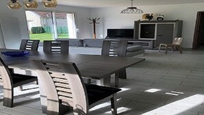 A modern living room with a dining table, chairs, a sofa, a TV, and a cabinet. - House in the hollow of the Embryenne valley. (Boubers les hesmond (62990))