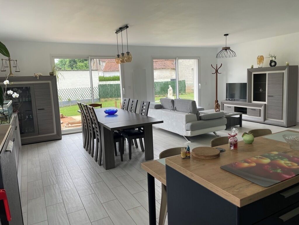 A modern kitchen with a dining area, a sofa, and a TV.