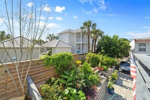 A residential area with a wooden deck, various potted plants, and a two-story house with a balcony. - Back to the Beach (Miramar Beach)