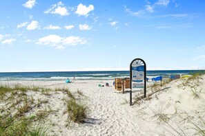 A sandy beach with a signpost, beach umbrellas, and a clear sky. - Back to the Beach (Miramar Beach)