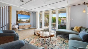 A modern living room with a large TV, a sofa, a coffee table, and a view of the outdoors. - Back to the Beach (Miramar Beach)