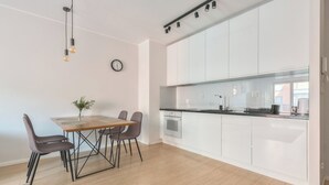A modern kitchen with white cabinets, a wooden dining table, and a clock on the wall. - Aura 39 by Grand Apartments (Gdansk)