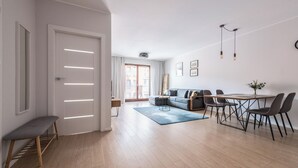 A modern living room with a sofa, dining table, and chairs. There is a bench and a small table with a vase of flowers. - Aura 39 by Grand Apartments (Gdansk)
