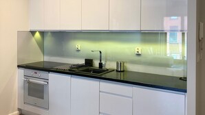 A modern kitchen with white cabinets, a black countertop, and a built-in oven. - Aura 39 by Grand Apartments (Gdansk)