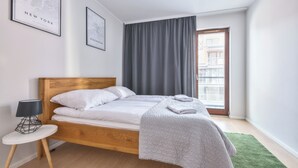A neatly made bed with a wooden headboard, a small bedside table with a lamp, and a framed map on the wall. - Aura 39 by Grand Apartments (Gdansk)