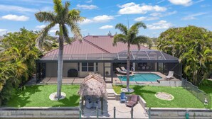 Ein modernes Haus mit Swimmingpool, einer überdachten Terrasse und einem strohgedeckten Gebäude.