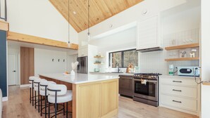 Een moderne keuken met een centraal eiland, barstoelen, roestvrijstalen apparatuur en houten keukenkastjes.