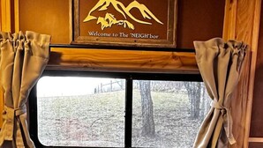 A cabin interior with a large window, curtains, and a sign reading "Welcome to The NEIGHBOR". - Custom HorseTrailerTinyHome near Grayson Highlands (Mouth of Wilson)