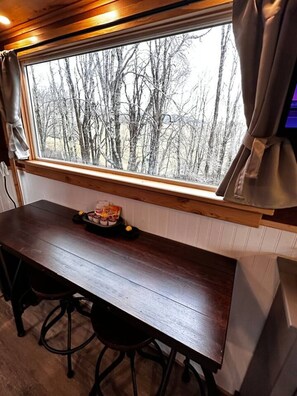 A wooden table with a window above it, a chair, and a small table with food items.