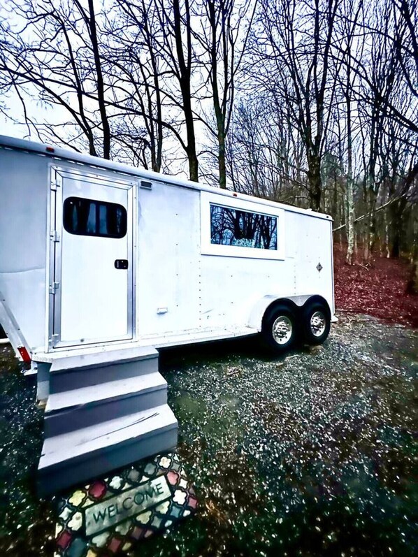 A white RV parked on a gravel path with a 'WELCOME' sign at the entrance.