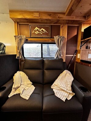 Un intérieur de camping-car chaleureux, avec un canapé en cuir, des rideaux et un panneau d’accueil.