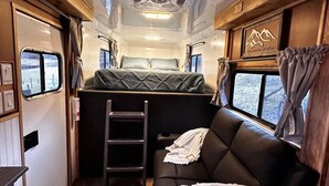 A compact RV interior with a kitchenette, a sleeping area with a sofa, and a small dining table. - Custom HorseTrailerTinyHome near Grayson Highlands (Mouth of Wilson)