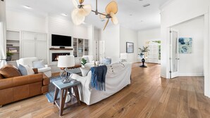 Un vaste salon comprenant un canapé en cuir marron, un divan blanc et une table basse. On y trouve également une cheminée, un téléviseur à écran plat et un ventilateur de plafond.