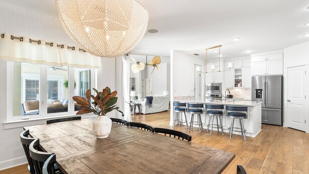 Une cuisine moderne avec des meubles blancs, des appareils en acier inoxydable et une table à manger en bois, accompagnée de chaises.