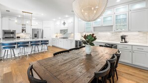 Une cuisine moderne avec des meubles blancs, une table à manger en bois et un luminaire suspendu.