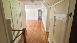 Un pasillo con suelo de madera, paredes blancas y puertas que dan a otras habitaciones.