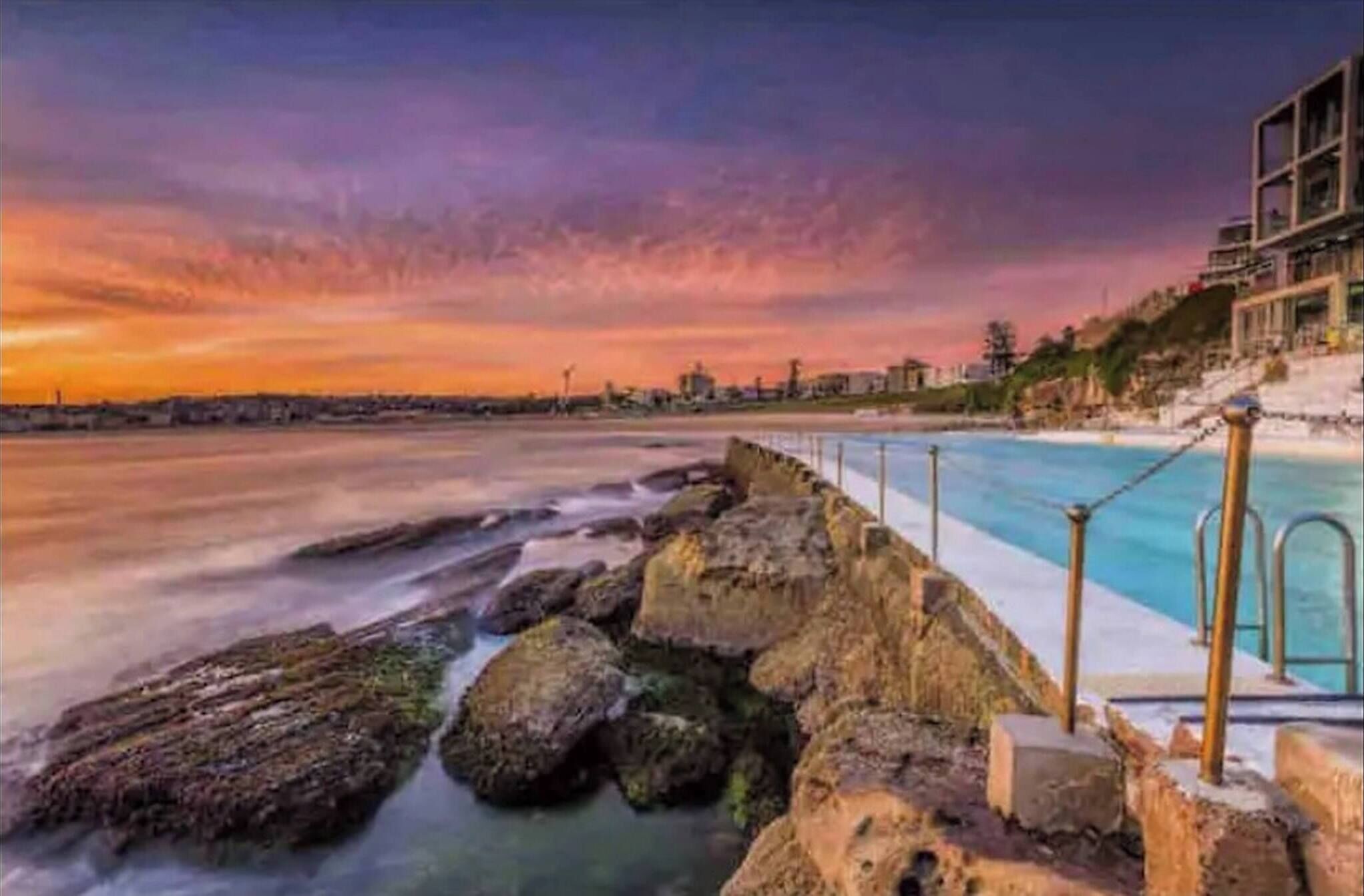 A coastal scene with a rocky shoreline, a swimming pool, and a building in the background.