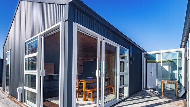 A modern building with large glass doors leading to an interior with wooden furniture and a dining area. - Mountain Haus - Ohakune Holiday Home (Ohakune)