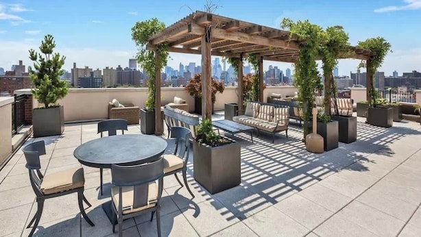 A rooftop patio with a pergola, seating area, and potted plants.