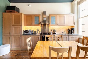 Een keuken met houten kastjes, een centraal geplaatst fornuis en een eettafel met stoelen.