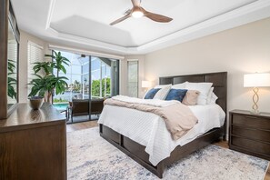 Une chambre dotée d’un grand lit, d’un ventilateur de plafond, d’une table de chevet, d’une lampe et offrant une vue sur la piscine à travers la porte vitrée.