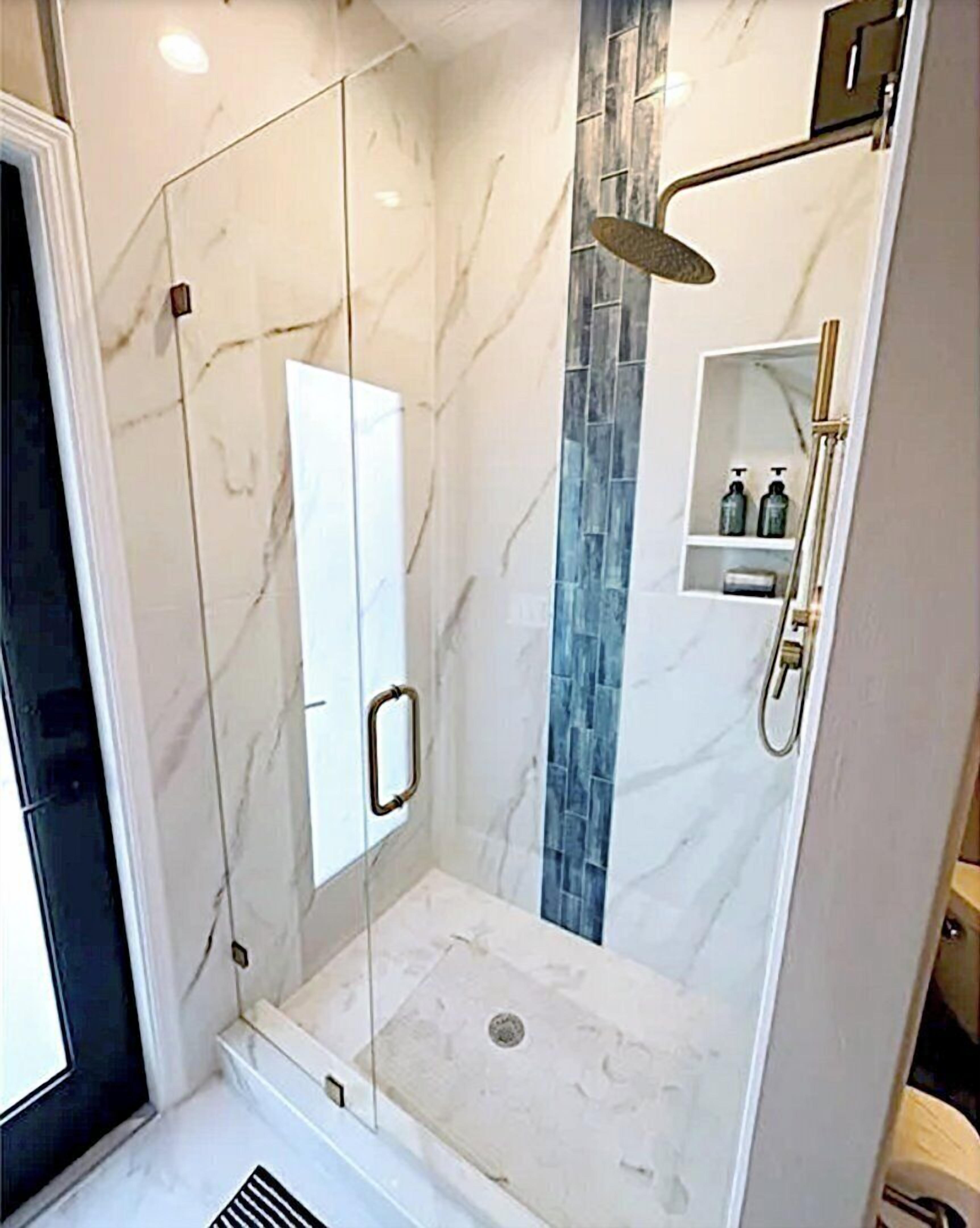 Eine moderne Dusche mit Glastüren, einem Marmorboden und einer blauen Fliesenwand.