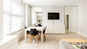A modern dining area with a white table, black chairs, and a flat-screen TV mounted on the wall. - Stylish Bayswater Flat with Outdoor Space (London)