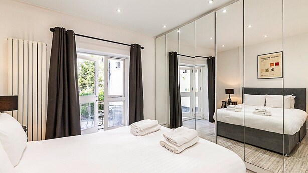 A modern hotel room with a large bed, a balcony, a mirrored wardrobe, and a view of the outdoors. - Stylish Bayswater Flat with Outdoor Space (London)