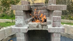 Un foyer extérieur en pierre, doté d’une grille en métal, entouré d’une bordure en béton.