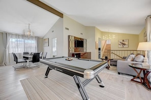 Uma sala de estar moderna com mesa de bilhar, um sofá, uma TV e uma escadaria.