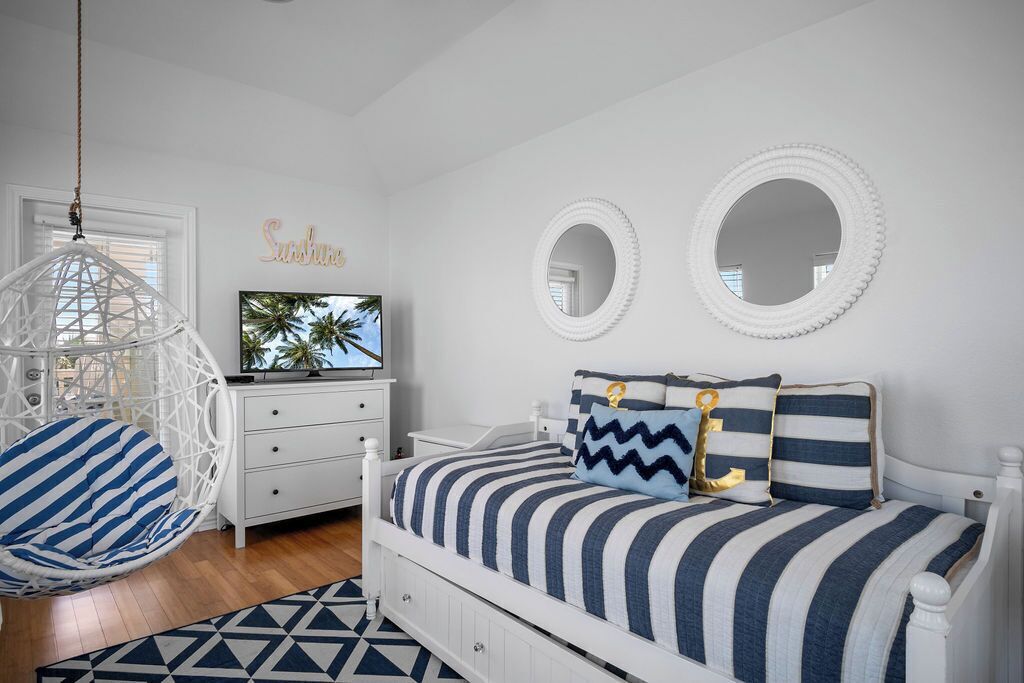 Ein Schlafzimmer mit Bett, Hängesessel, Kommode und zwei Wandspiegeln.