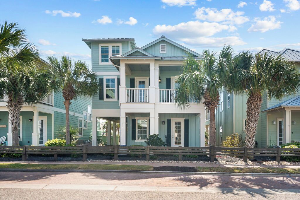A two-story house with a balcony, surrounded by palm trees.