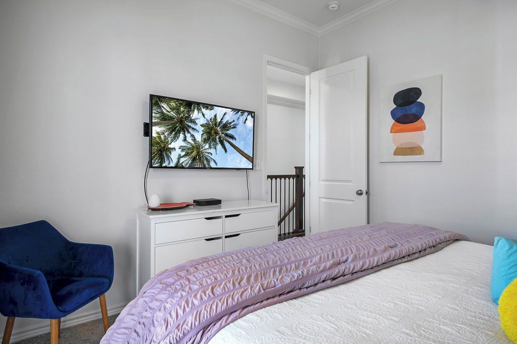 A bedroom with a bed, a desk with a computer, a chair, and a door.