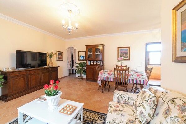 A living room with a television, a dining table with chairs, a sofa, and a cabinet.