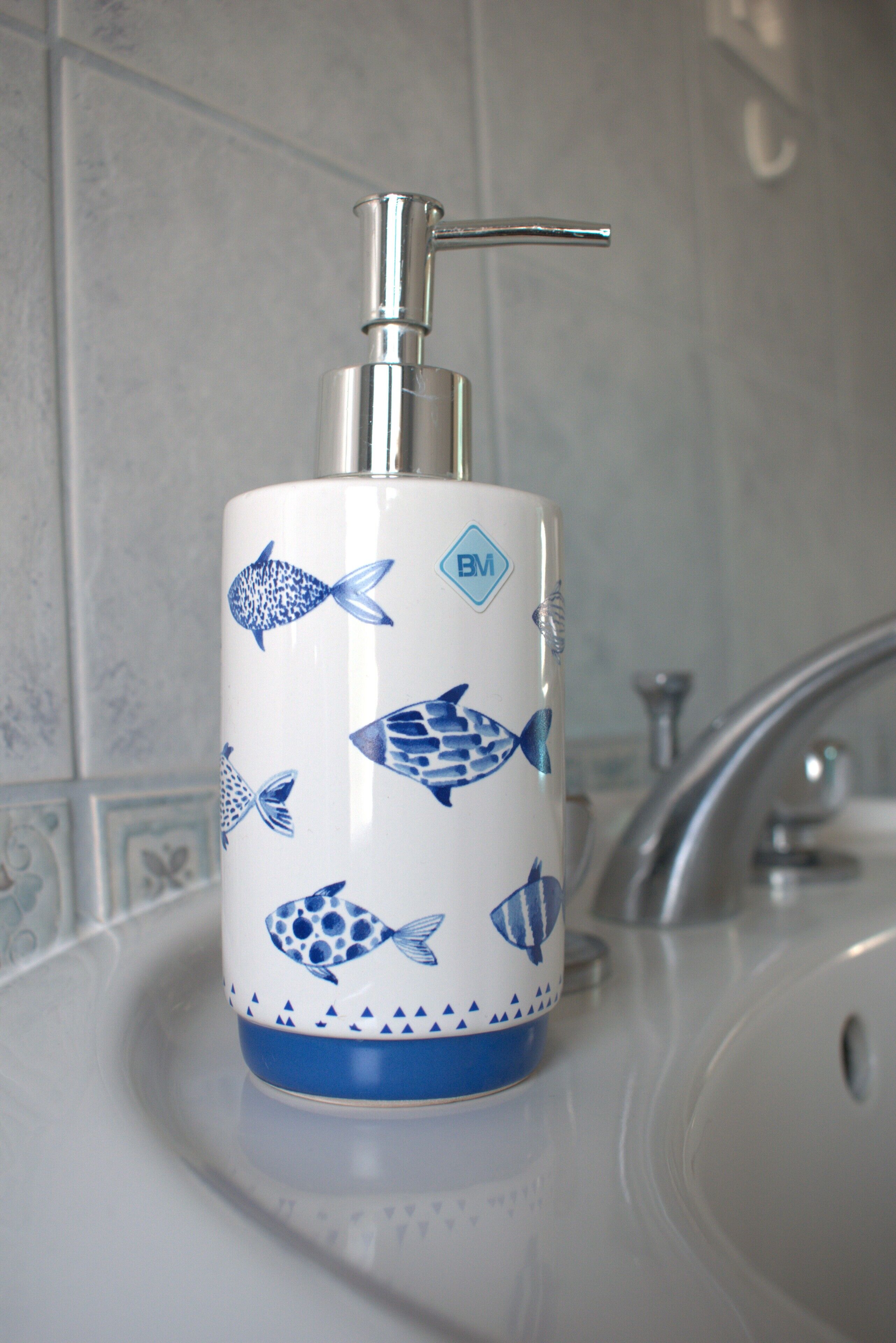 A bathroom sink with a white and blue fish-patterned soap dispenser.