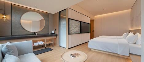 Ein modernes Hotelzimmer mit einer Couch, einem Bett, einem runden Tisch und einem großen Spiegel.