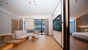 A modern hotel room with a sofa, a small round table, a bed, and a large TV. - Madison Hot Spring Hotel Jian Wugong Mountain (Ji'an)