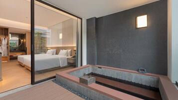 A modern hotel room with a large bed, a glass partition, and a stone bathtub.