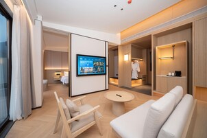 Una habitación de hotel moderna con un televisor de pantalla plana grande, un sofá, una silla, una mesa redonda y un vestidor.