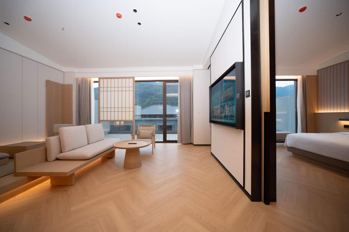 A modern hotel room with a sofa, a small round table, a bed, and a large TV.