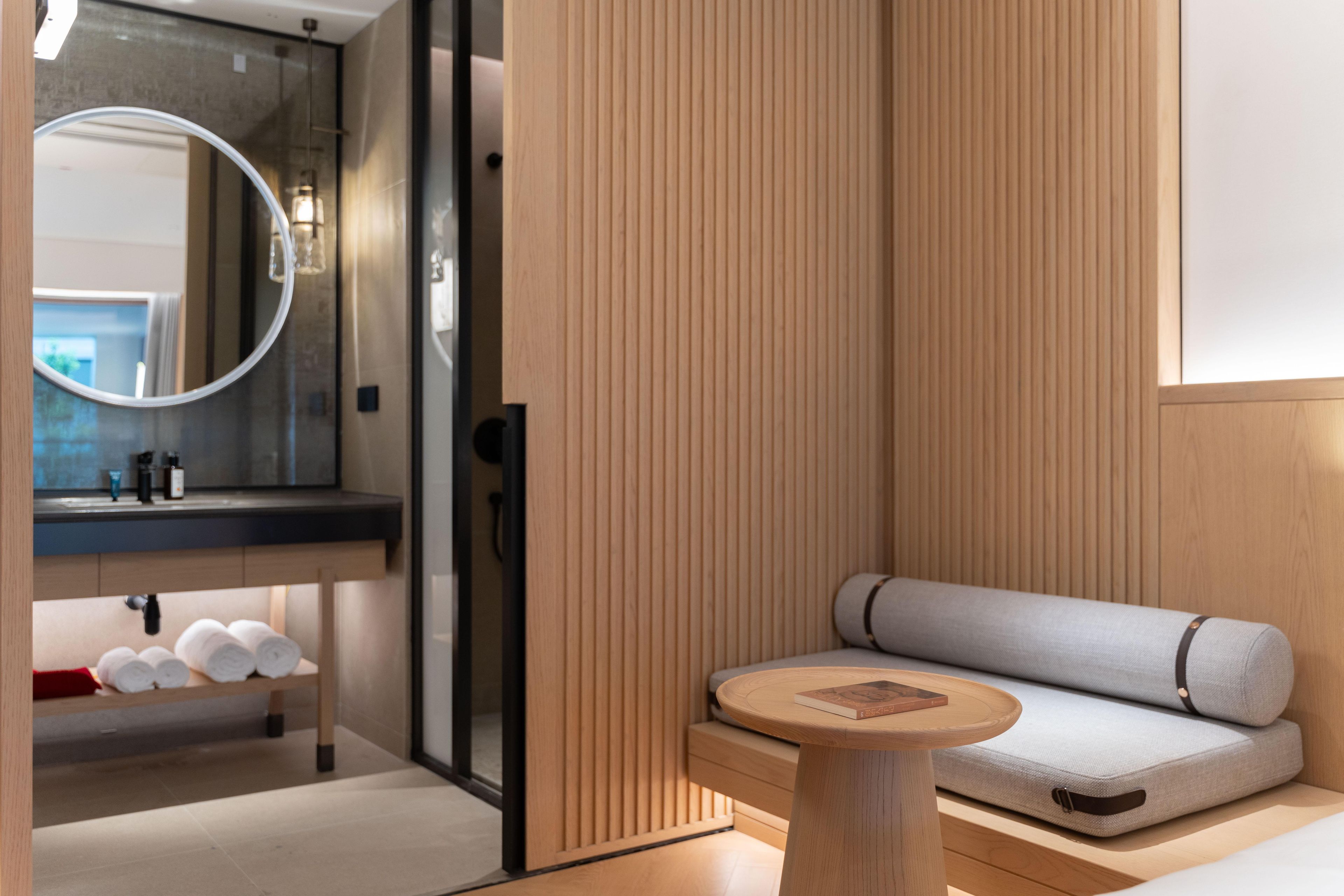 Un baño moderno con tocador de madera, espejo redondo y zona de estar integrada con perchero.