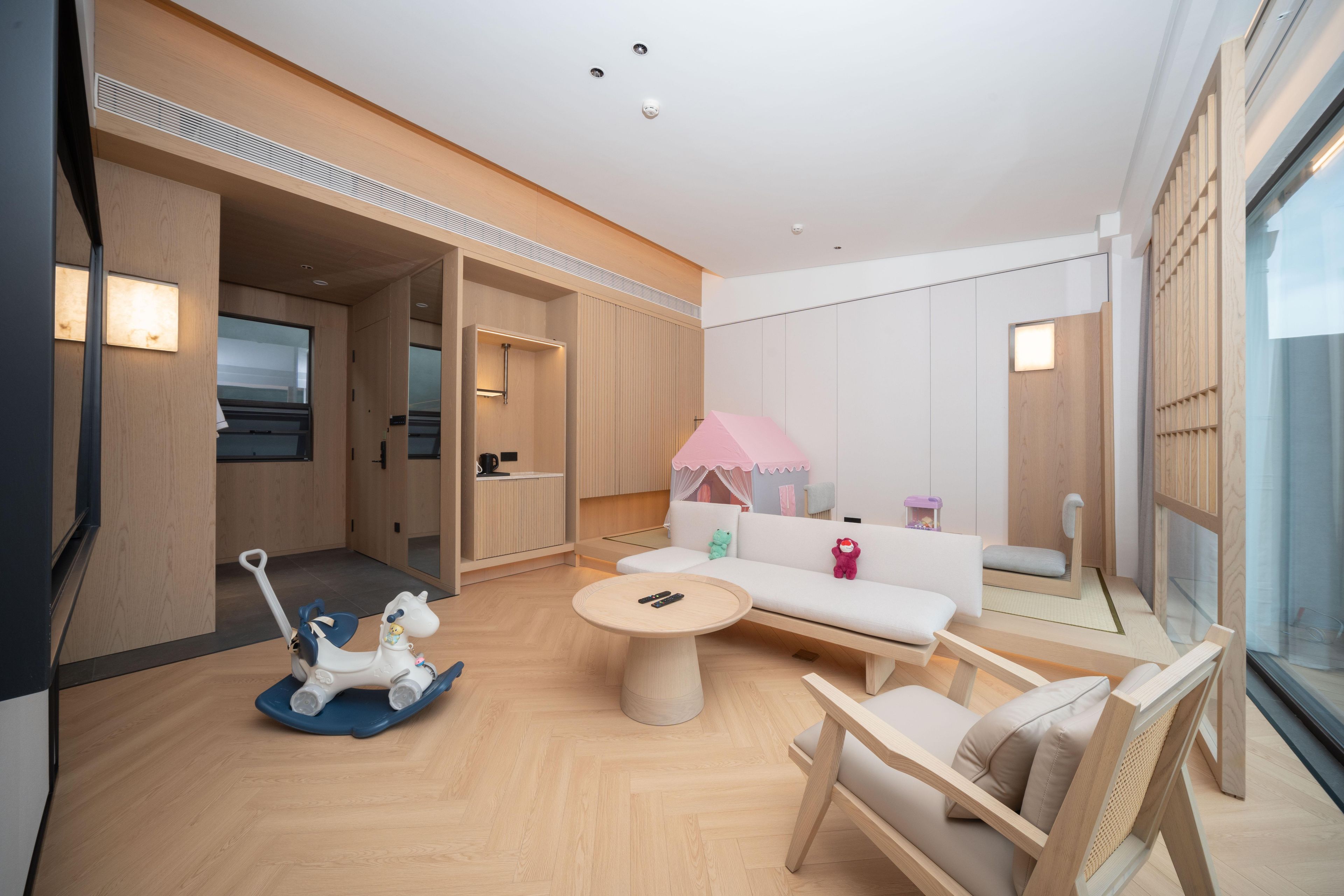 Una habitación moderna y bien iluminada con piso de madera, una mesa redonda, un sofá y una silla. Hay un televisor a la izquierda y una ventana a la derecha.