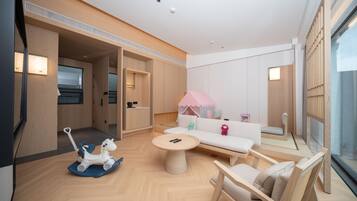 Una habitación moderna y bien iluminada con piso de madera, una mesa redonda, un sofá y una silla. Hay un televisor a la izquierda y una ventana a la derecha.