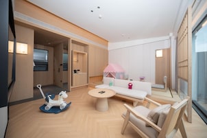 Una habitación moderna y bien iluminada con piso de madera, una mesa redonda, un sofá y una silla. Hay un televisor a la izquierda y una ventana a la derecha.